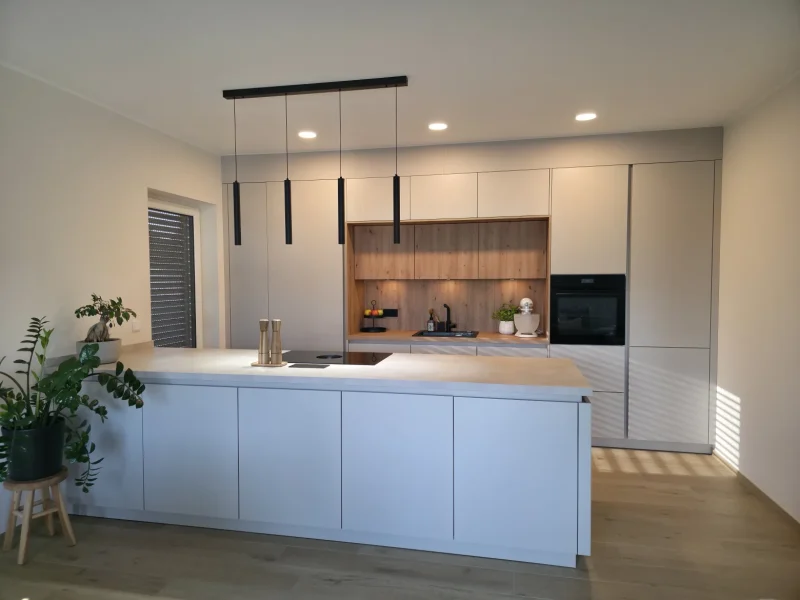 Moderne, helle Küchen mit weißen Schränken, großem Inselblock, schwarzen Pendelleuchten und eingebautem Ofen. Wandelbar und zeitlos schön dank Holzrückwand, minimalistischem Dekor und heller Beleuchtung durch Deckenstrahler.