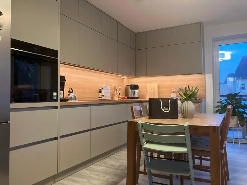 Moderne, wandelbar Küche mit hellen Holzschränken und Arbeitsplatten, einem hölzernen Esstisch mit drei Stühlen, einer Blumenvase und einer Einkaufstasche auf dem Tisch. Ein Fenster auf der rechten Seite füllt diesen zeitlos schönen Raum mit natürlichem Licht.