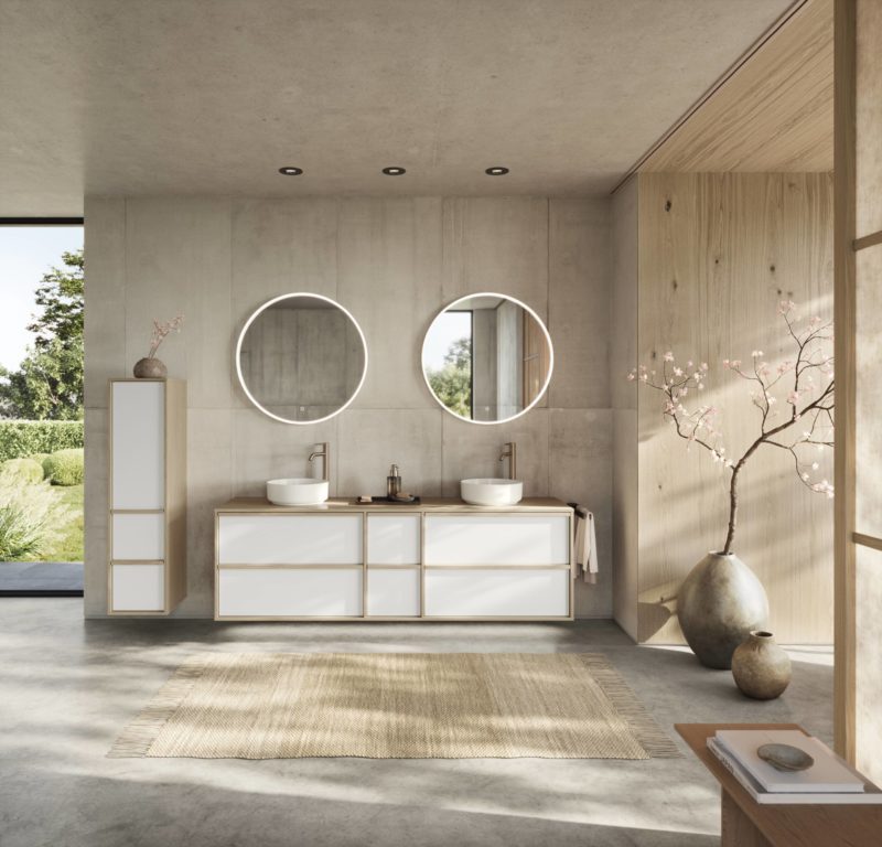Ein modernes Badezimmer mit zwei runden Spiegeln, Aufsatzwaschbecken und Holzakzenten, das an die klaren Linien erinnert, die für den unverwechselbaren Stil von Studio Leipzig charakteristisch sind. Durch ein großes Fenster blickt man auf die grüne Natur, die wie ein ruhiger Spielplatz wirkt. Zur minimalistischen Einrichtung gehören ein hoher Schrank, ein gewebter Teppich und eine Vase mit blühenden Zweigen.