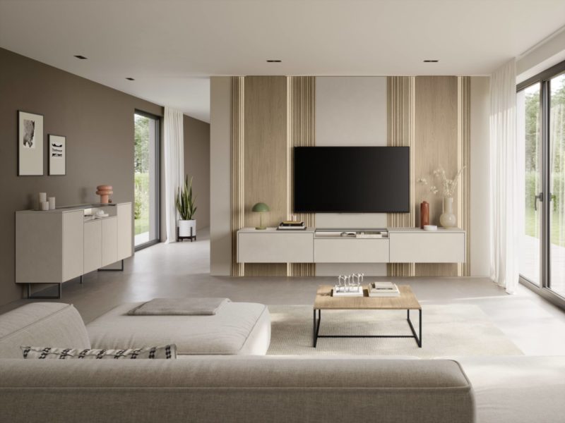 Ein modernes Wohnzimmer in neutralen Farbtönen, mit einem großen Wandfernseher, minimalistischen Möbeln, einem Couchtisch und großen Fenstern, durch die Tageslicht hereinströmt – dieser einladende Raum im Studio Leipzig wirkt wie der perfekte Ort zum Entspannen. Zur Dekoration gehören Pflanzen, Vasen und gerahmte Kunstwerke an den Wänden.