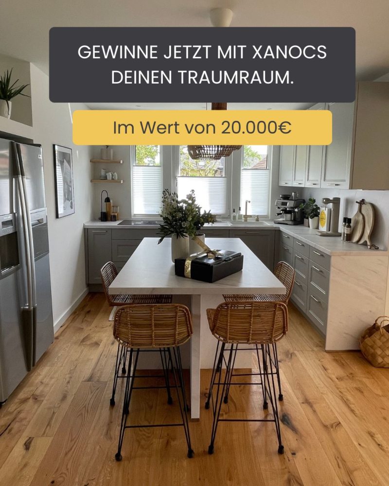 Moderne Küche mit weißen Schränken, einer zentralen Kücheninsel mit drei Barhockern, Holzböden und Zierpflanzen. Der Text im Bild wirbt für ein Gewinnspiel, bei dem Sie die Chance haben, mit Xanocs einen Traumraum im Wert von 20.000 € zu gewinnen.