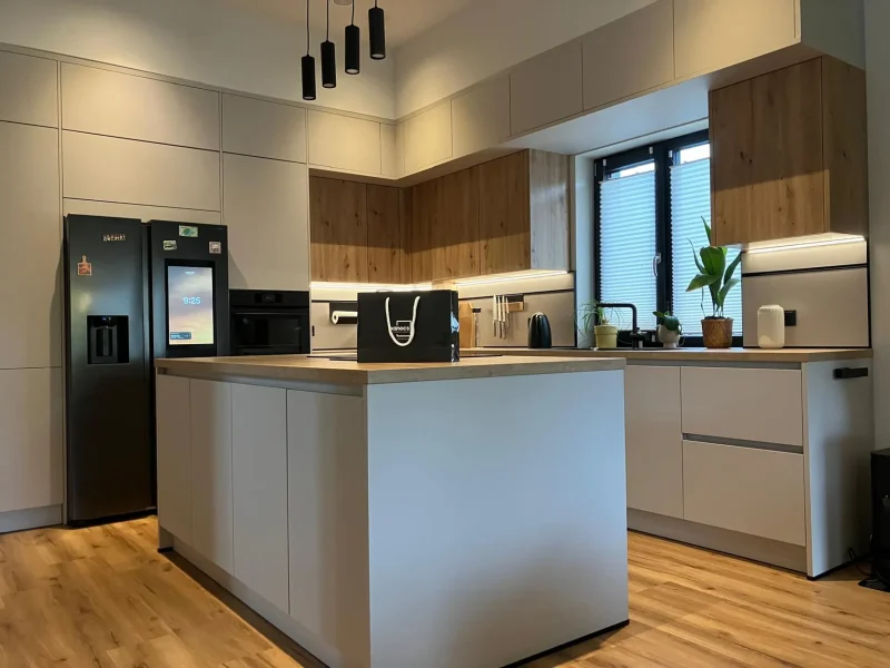 Moderne Küche mit Kochinsel, Einbaugeräten, Holz- und weißen Schränken, schwarzem Kühlschrank, verschiedenen Kleingeräten, einem Fenster mit Jalousien und einer schwarzen Pendelleuchte – entdecken Sie mit Immscout neue Möglichkeiten für Ihr neues Zuhause.