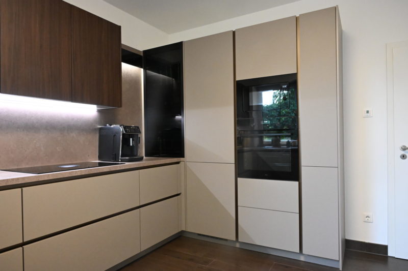 Moderne Küche mit dunklen Holzoberschränken, hellbeigen Unterschränken, einem Einbaubackofen und einer Kaffeemaschine auf der Arbeitsplatte – für einen perfekten Küchenneustart.