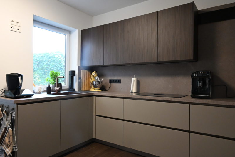 L-förmige Küche für einen Küchenneustart mit Oberschränken aus dunklem Holz, mattgrauen Unterschränken, einer Eckspüle und modernen Geräten auf der Arbeitsplatte.