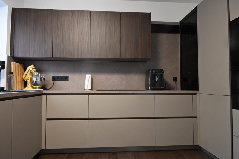 Moderne Küche mit Oberschränken aus dunklem Holz, Unterschränken in hellem Taupe, einer Kaffeemaschine auf der Arbeitsplatte und einer Küchenmaschine – ideal für eine gemütliche Wohlfühlküche.